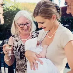 Elegancka stylizacja na chrzciny: matka karmi dziecko w białej sukience, babcia z kieliszkiem wina, dziadek obok.