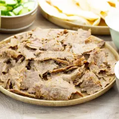 Pyszny kebab z piekarnika na talerzu, otoczony świeżymi warzywami, sosem i plackami. Idealny na domowy obiad.