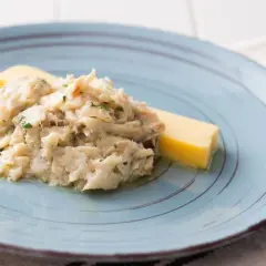 Baccalà alla Vicentina, ein cremiges Stockfischgericht mit Petersilie, serviert mit einem Stück Polenta auf einem blauen Teller.