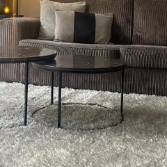 Gemütliches Wohnzimmer mit einem Sofa in greige Farbe, zwei Marmor-Couchtischen und einem flauschigen Teppich.