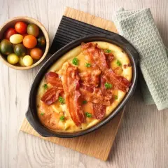 En härlig tjockpannkaka med knaprigt bacon, toppad med persilja. Bredvid en skål med färgglada körsbärstomater.