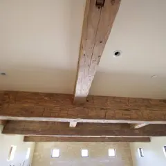 Poutres apparentes en bois ciré, patinées par le temps, soutenant un plafond blanc avec des spots encastrés.