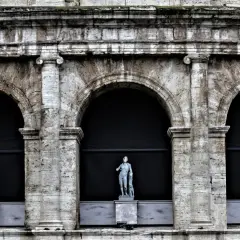 Tre statue classiche emergono dall'ombra di un imponente arco a Roma, testimoni silenziose di un passato glorioso.