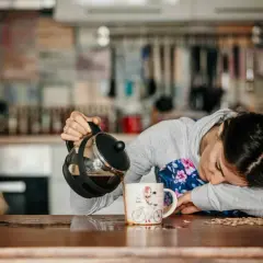 Une femme, visiblement à bout de forces, verse du café dans une tasse, le regard perdu. Un enfant la regarde, l'air intrigué. Elle semble tomber de fatigue.