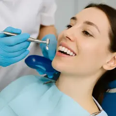 Uśmiechnięta kobieta podczas zabiegu fluoryzacji w ciąży. Dentysta w rękawiczkach wykonuje profesjonalny zabieg.