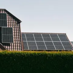 Panele słoneczne na dachu domu, zapewniające czystą energię. W tle las, a na pierwszym planie żywopłot. System jest też zabezpieczony odgromnikiem.