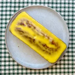 Un delicioso bizcocho de mango y yogur, cubierto con un glaseado amarillo brillante, descansa sobre un plato gris.