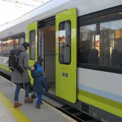Matka z dzieckiem wsiada do pociągu na stacji Bydgoszcz. Zielona góra na pociągu symbolizuje ekologiczny transport.