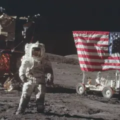 Astronaut w skafandrze podczas spaceru po księżycu, obok lądownika i łazika z amerykańską flagą.