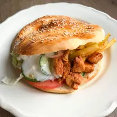 Kebab w bułce z kurczakiem, frytkami, warzywami i sosem na białym talerzu.