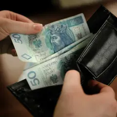 Ręce wkładają polskie banknoty 50 zł do czarnego portfela. To kieszonkowe dla dziecka na drobne wydatki.