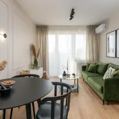 Nowoczesne mieszkanie w bloku z zieloną kanapą, czarnym stołem i designerską lampą.