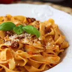 Pyszne tagliatelle bolognese z parmezanem i listkami bazylii na białym talerzu.