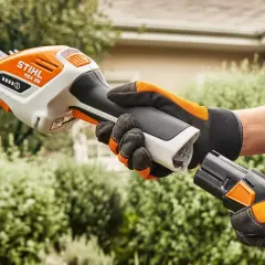 Ręka w rękawicy zakłada baterię do nożyc akumulatorowych do trawy Stihl HSA 26, gotowa do przycinania.