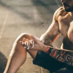 Ein Mann mit beeindruckenden herren tattoos bereitet sich mit Magnesium vor. Kettlebells liegen im Hintergrund.