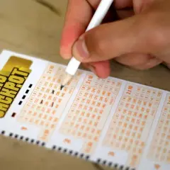 Dłoń z ołówkiem zaznacza liczby na kuponie Eurojackpot.