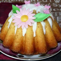 Babka jogurtowa cytrynowa ozdobiona lukrem, różowym kwiatkiem i motylkami. Idealna na wiosenne popołudnie.