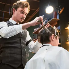 Elegancki barber z wąsikiem precyzyjnie ścina włosy klienta. Kto to? Mistrz fryzjerstwa!
