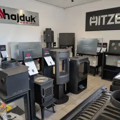 Nowoczesny piec koza z żeliwnymi elementami i szklanymi drzwiczkami, prezentowany w salonie kominkowym.
