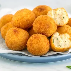 Arancini dorati e croccanti, perfetti per gustose ricette con ricotta. Uno è morso, rivelando un ripieno morbido e saporito.