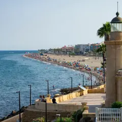 Faro y playa abarrotada en el paseo marítimo de Roquetas de Mar. Gente disfrutando del sol y el mar.