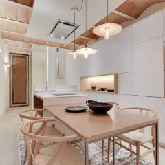 Cocina moderna con pared de piedra, isla central y lámparas alargadas colgantes sobre mesa de madera.