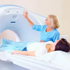 Pacjentka na stole rezonansu magnetycznego, pielęgniarka obsługuje aparat.