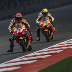 Dos pilotos de MotoGP compiten en una carrera. El piloto número 93 de Repsol Honda lidera, seguido de cerca por el piloto número 36. El coste de una moto de MotoGP es altísimo.