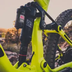 Close-up of a bright yellow mountain bike's rear suspension. The Rock Shox Super Deluxe shock has a length chart visible.
