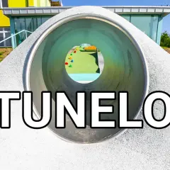 Widok przez tunel z placu zabaw na kolorowe elementy i budynek.