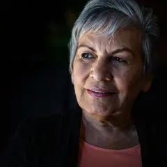 Portret starszej kobiety z siwymi włosami, patrzącej w bok z lekkim uśmiechem.
