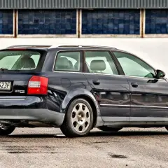 Ciemnogranatowe Audi A4 B6 1.9 TDI Avant stoi na mokrym asfalcie przed budynkiem z niebieskimi oknami.
