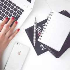 Karta pracy na biurku: dłoń na klawiaturze laptopa, obok telefon, notatnik i długopis.