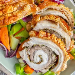 Knusprige Porchetta, ein italienischer Schweinebraten, wird mit karamellisierten Karotten, Sellerie und roten Zwiebeln serviert.