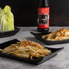 Dwa talerze z aromatyczną, kapustą pekińską na ciepło, doprawioną płatkami chili. Obok butelka sosu ostrygowego.