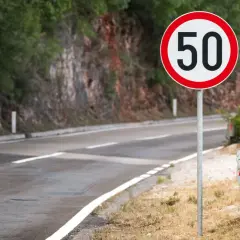Znak drogowy B-33 z cyfrą 50 na tle drogi i skalistego zbocza.