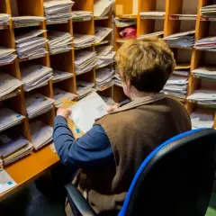 Pracownica sortuje listy w pocztowym regale. Zastanawia się, ile czasu na odebranie awizo, zanim zaginie w gąszczu przesyłek.