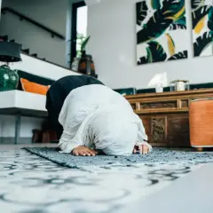 Kobieta w hidżabie wykonuje modlitwę codzienną na dywaniku w przestronnym, nowoczesnym wnętrzu.