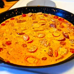 En krämig korv stroganoff deluxe i en stekpanna, med skivad korv och körsbärstomater i en gyllene sås.