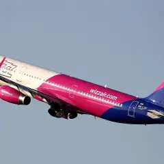 Samolot Wizz Air w różowo-niebieskich barwach wznosi się na tle błękitnego nieba.
