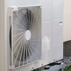 Unité extérieure d'une pompe à chaleur à installer soi même, posée sur des pieds métalliques près d'un mur.