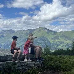 Familj njuter av en fantastisk utsikt under en bad gastein vandring. Barnen pekar ut över de gröna bergen och molnen.