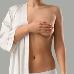 Kobieta w białym szlafroku zakrywa dłonią swoje małe piersi.