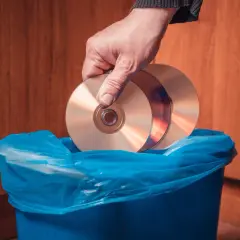 Dłoń wrzuca płyty CD do niebieskiego kosza. Zastanawiasz się, gdzie wyrzucić płyty GK?