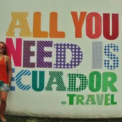 Uśmiechnięta turystka w Vilcabamba pozuje na tle kolorowego napisu "All you need is Ecuador. Travel".