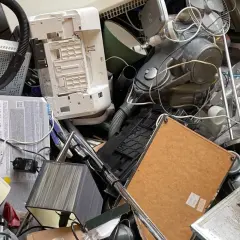 Stos starych urządzeń elektronicznych: drukarka, odkurzacz, wentylator, lampa.