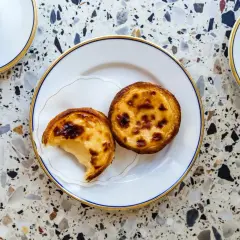 Dwa pyszne pastel de nata na talerzyku, obok filiżanki kawy. Idealny deser na popołudnie.