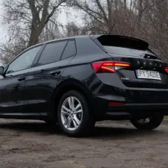 Czarna Skoda Fabia 2024 z polskimi tablicami rejestracyjnymi stoi na brudnej drodze, otoczona drzewami.