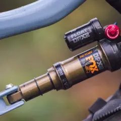 Close-up of a blue bicycle frame with a gold and black Fox Float DPX2 Factory shock. The shock has "FACTORY" and "DPX2" branding.