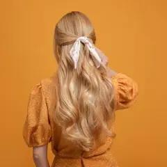 Chevelure blonde ondulée, coiffée en demi-queue avec un foulard fleuri, sur fond orange.